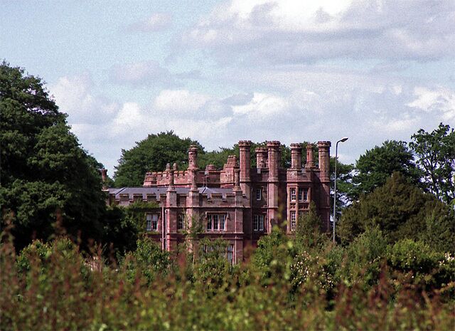 A large, historic building with multiple chimneys and surrounded by lush greenery.