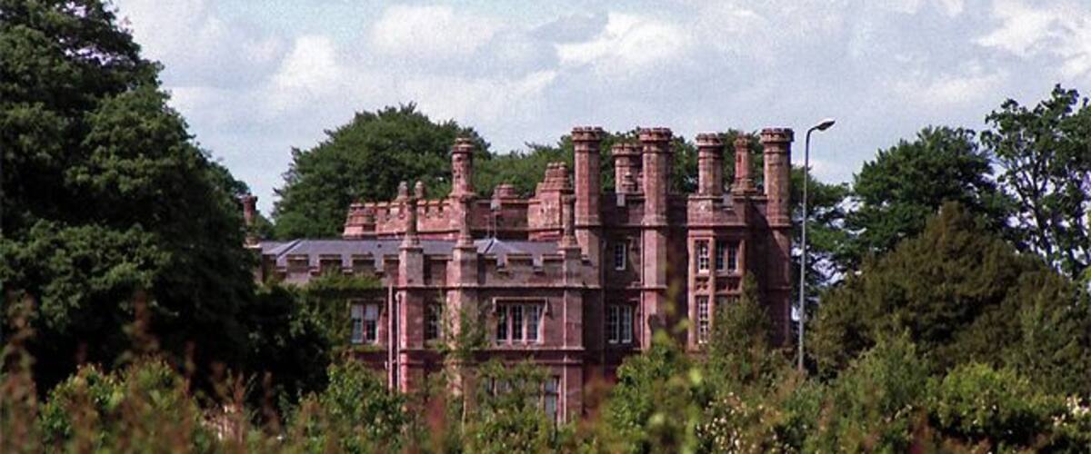 A large, historic building with multiple chimneys and surrounded by lush greenery.