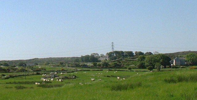 A rural landscape with green fields, scattered sheep, and a few buildings in the distance.