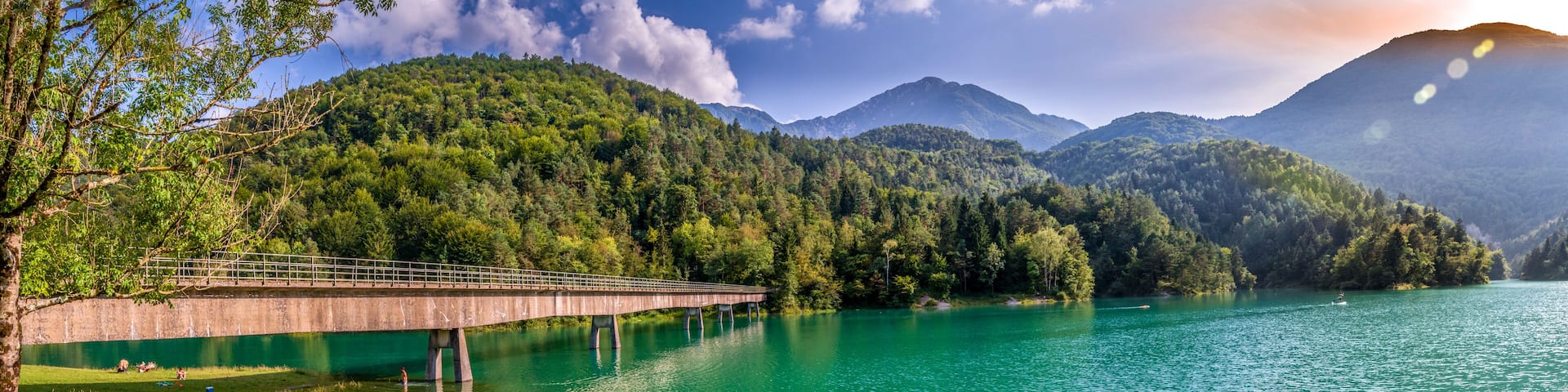 A bridge over a turquoise lake surrounded by forested mountains.