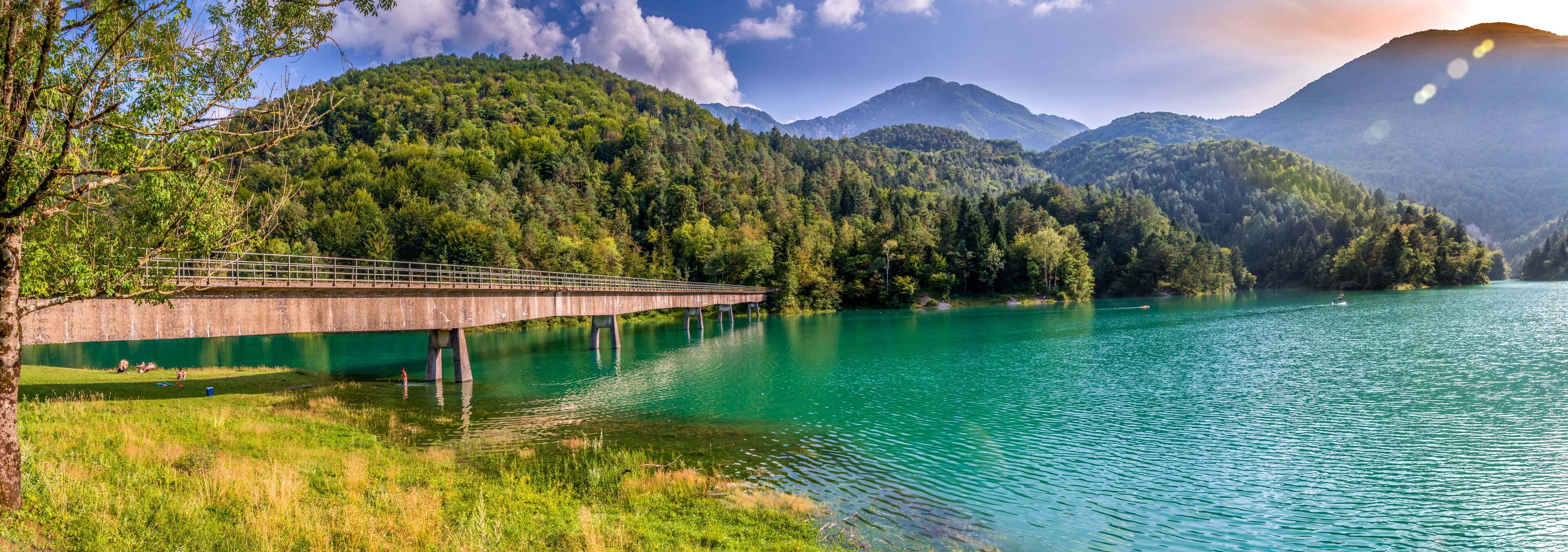 A bridge over a turquoise lake surrounded by forested mountains.