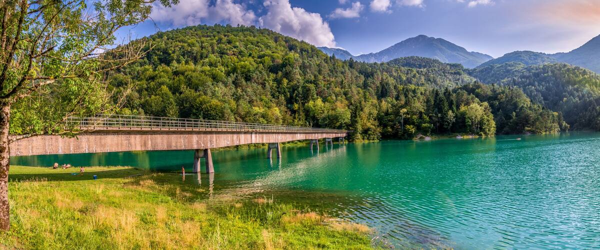 A bridge over a turquoise lake surrounded by forested mountains.