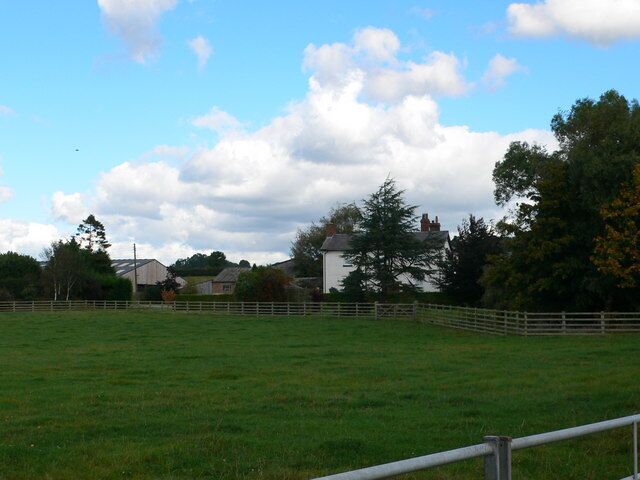 A grassy field with a white fence, a white building, and trees in the background.