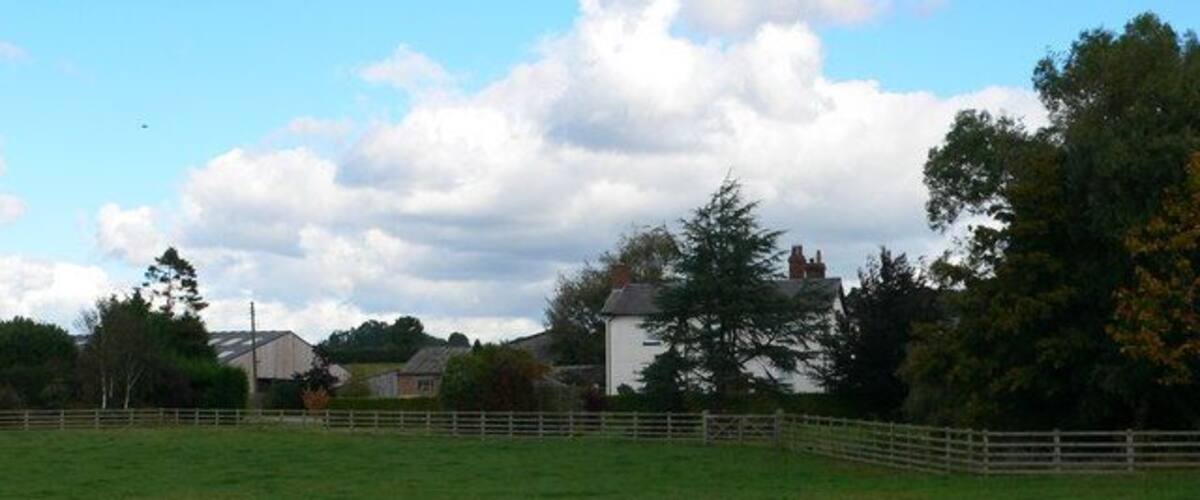 A grassy field with a white fence, a white building, and trees in the background.