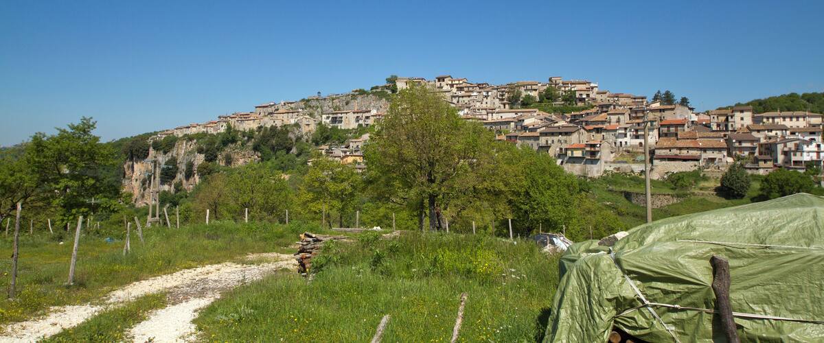 A hillside village with buildings, a dirt path, and greenery.