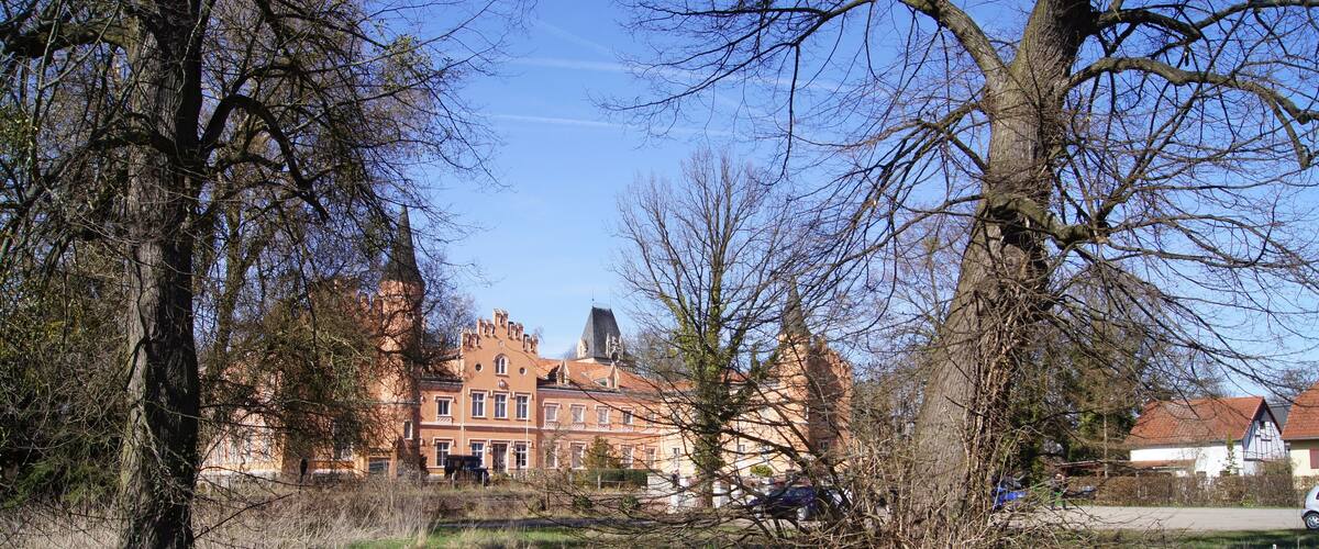 A park with trees, grass, and a large brick building with a tower.