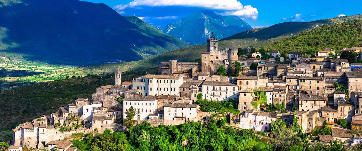 A historic town with medieval architecture, surrounded by lush green hills and mountains.