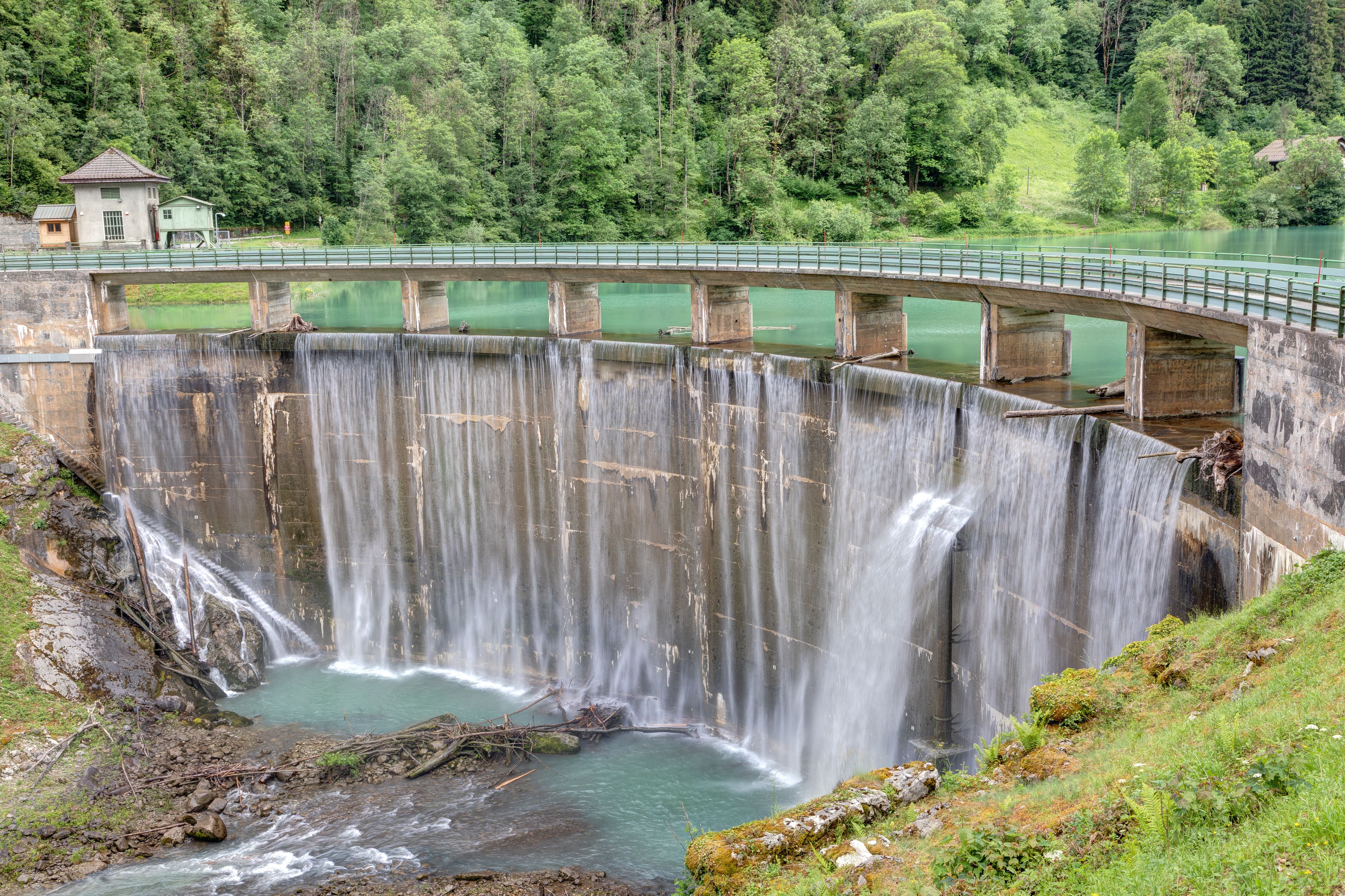 Una presa amb un pont, una cascada i un turó forestal.