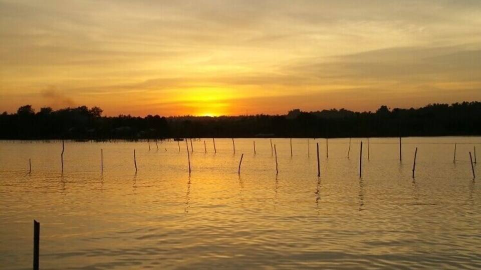 A sunset over a calm lake with a dock and a boat.