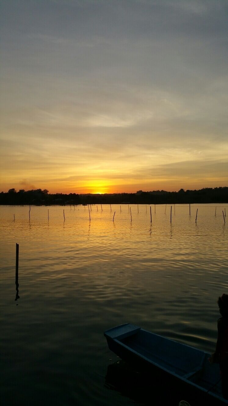 A sunset over a calm lake with a dock and a boat.
