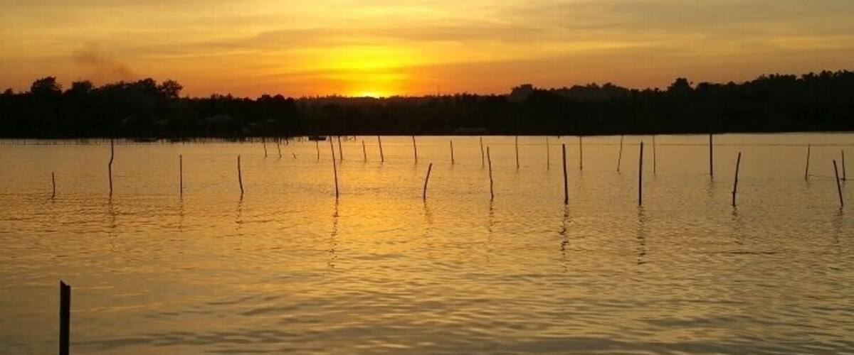 A sunset over a calm lake with a dock and a boat.