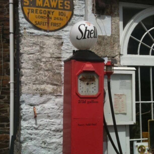 A vintage gas pump with a Shell logo, a sign reading "S. MAWES, TREGONY 101, LONDON 2631, SAFETY FIRST," and a 2/3rd gallon capacity indicator.