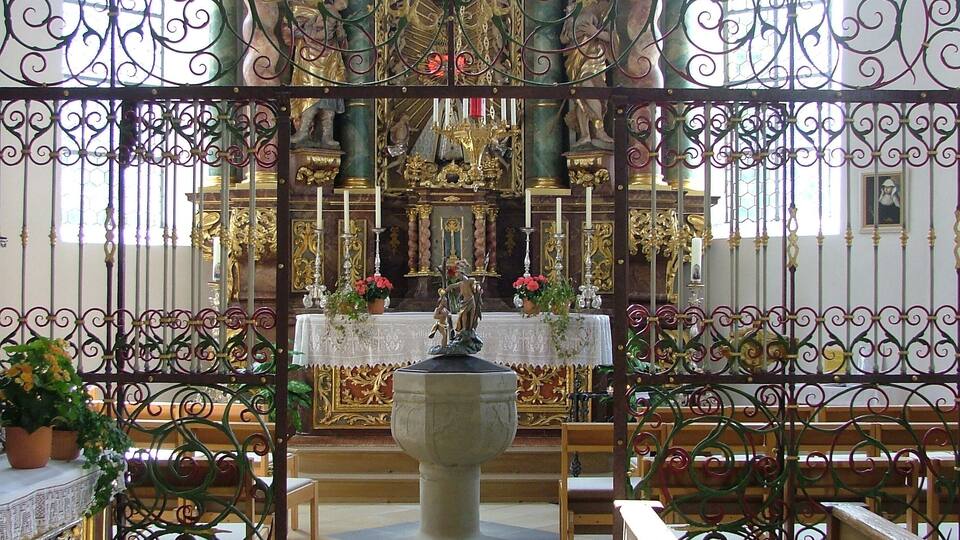 An ornate church interior with a central altar, pews, and decorative ironwork.