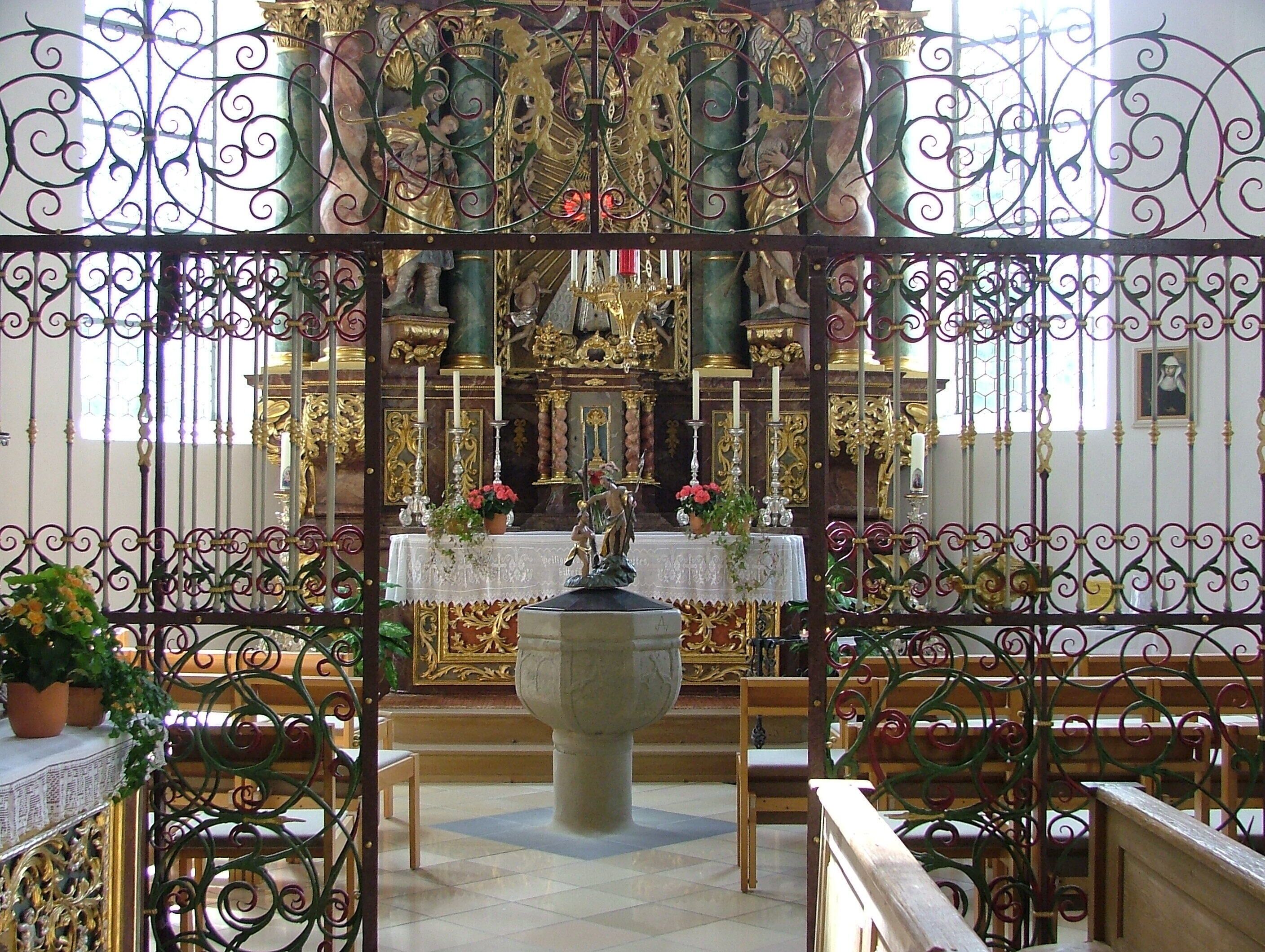 An ornate church interior with a central altar, pews, and decorative ironwork.