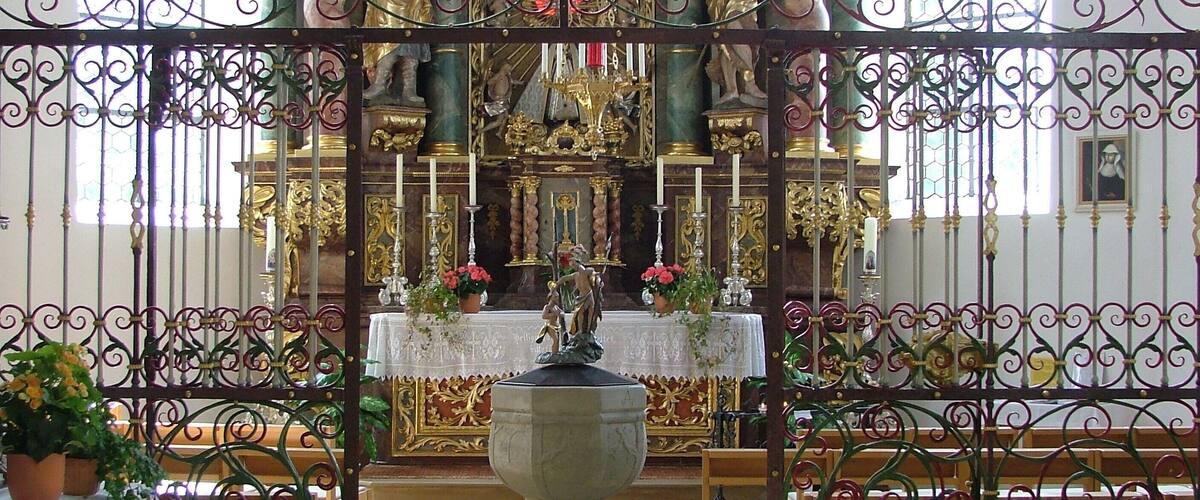An ornate church interior with a central altar, pews, and decorative ironwork.