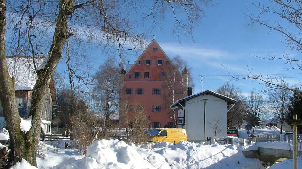 A snow-covered landscape with a large red building, a yellow van, and leafless trees.