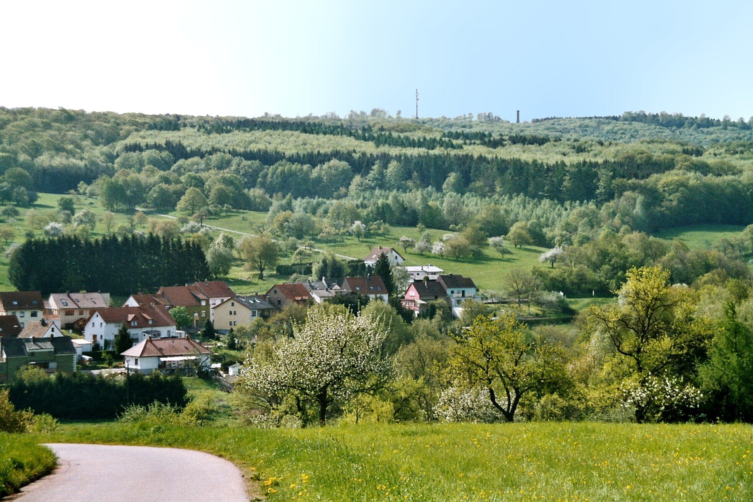 A rural landscape with rolling hills, a winding road, and a cluster of houses.
