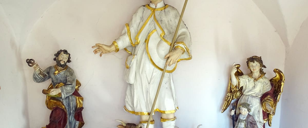 A religious statue with three figures, including a central figure holding a staff and two angels on either side.