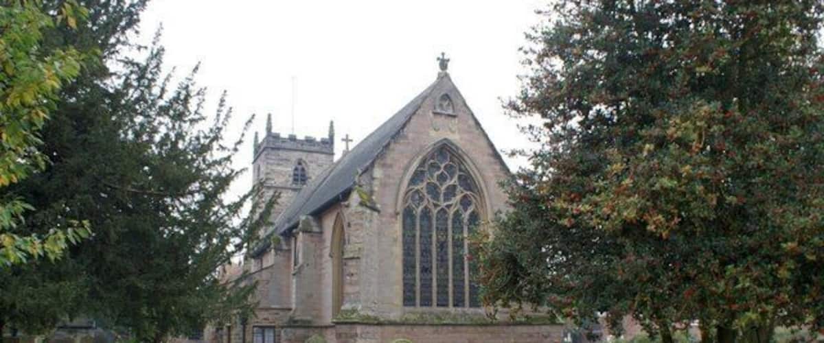 A church with a pointed steeple and large arched windows, surrounded by a cemetery with headstones.