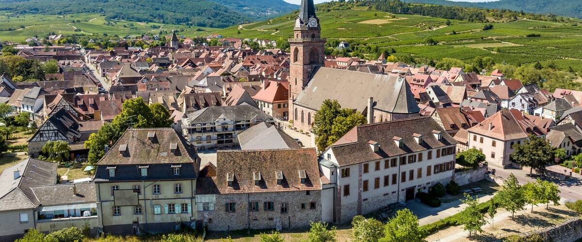 A historic town with a prominent church tower, surrounded by lush green hills and vineyards.