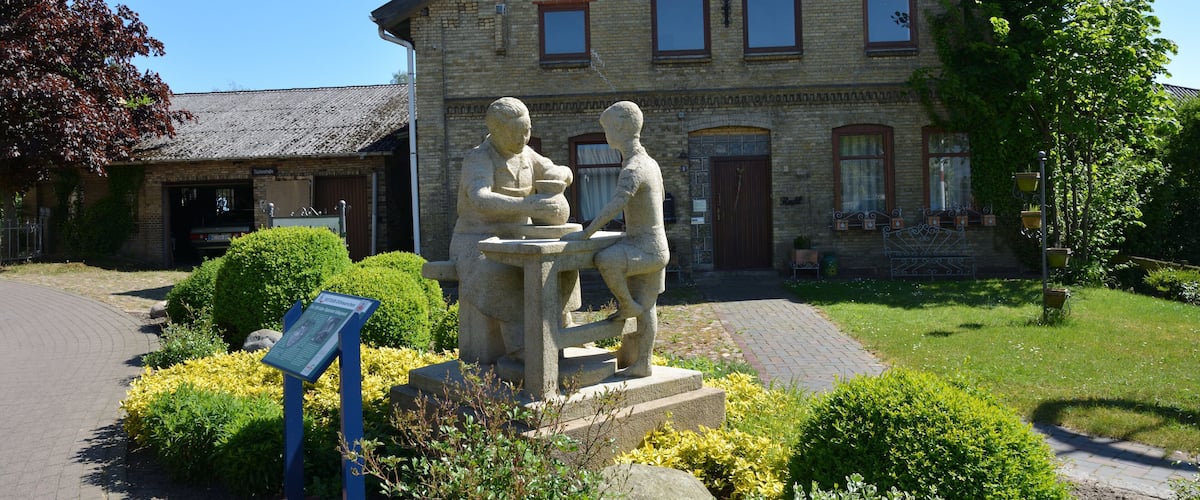 A stone statue of two figures in a garden in front of a brick building.