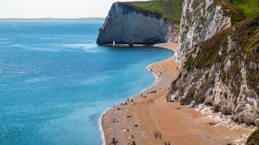 A coastal landscape with a sandy beach, a large cliff, and the sea.