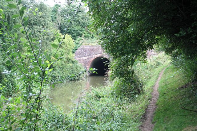 A narrow waterway with a brick bridge and lush greenery.
