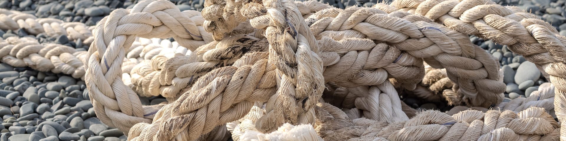 The ship's rope is in selective focus. Woven with thick bundles of threads, the ship's rope lies on a pebble beach. Türkiye, Samandağ, Hatay, Mediterranean coast.