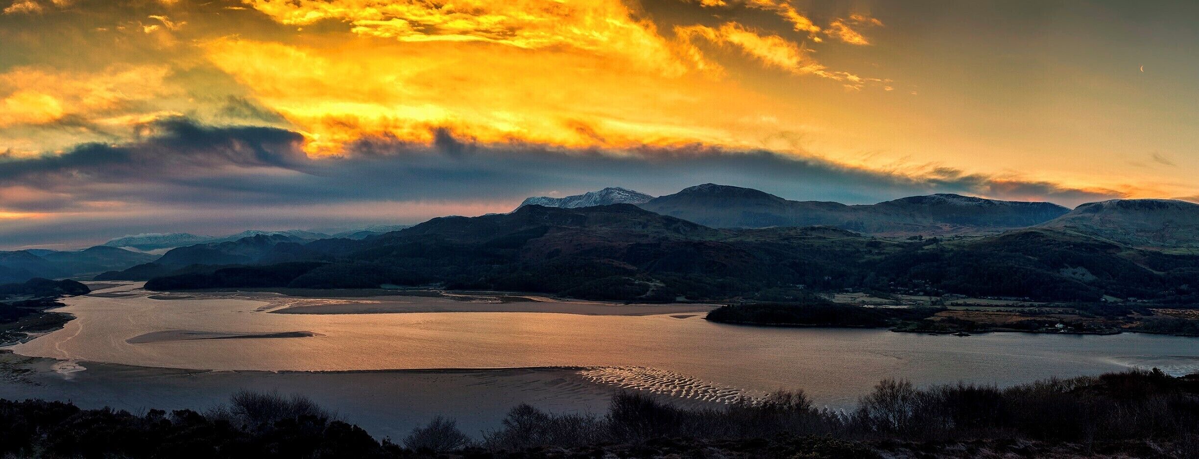A lake surrounded by mountains during sunset.