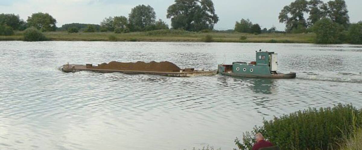 A barge on a river with a person fishing by the bank.