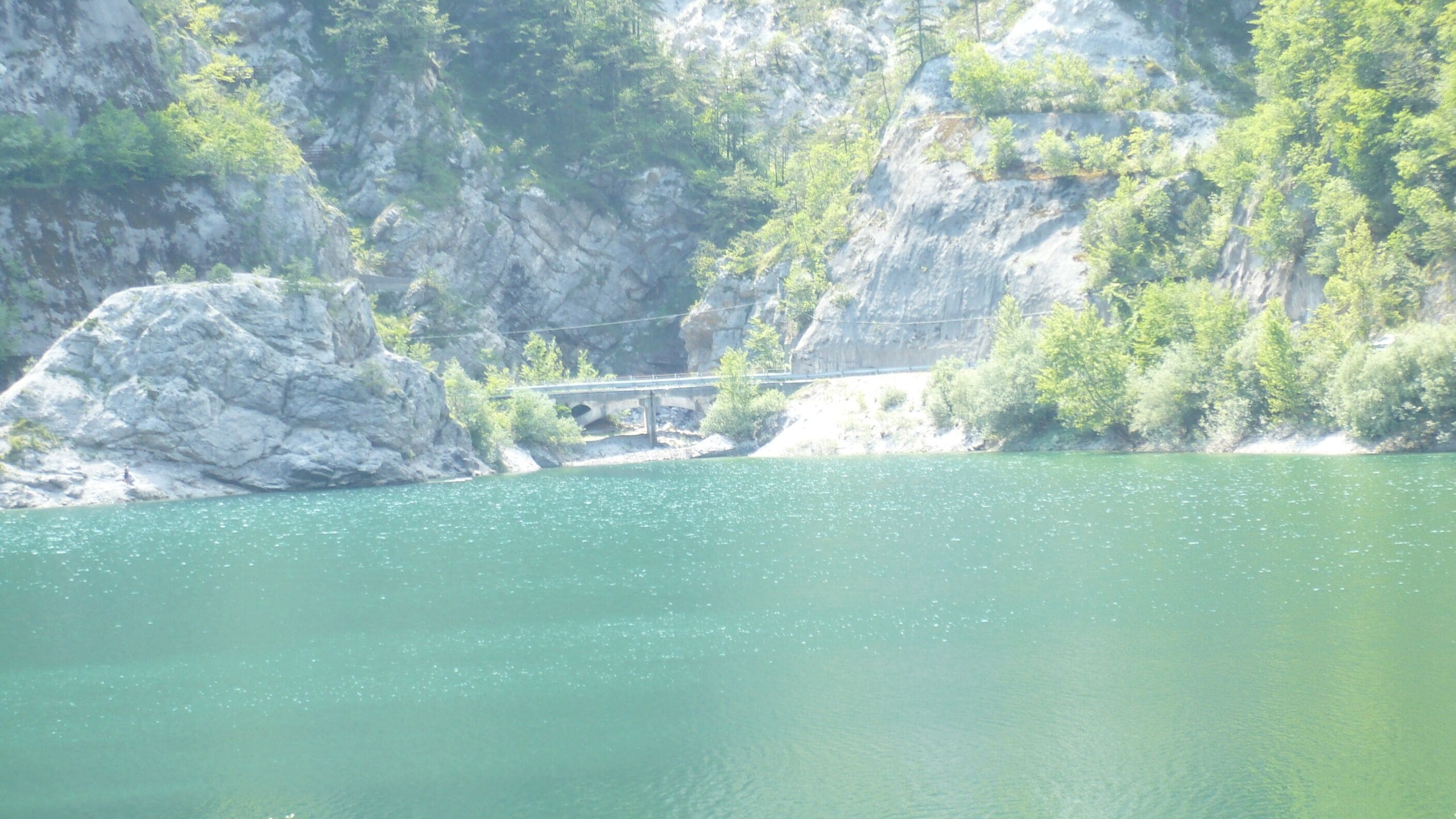 A bridge over a river with rocky cliffs and greenery.