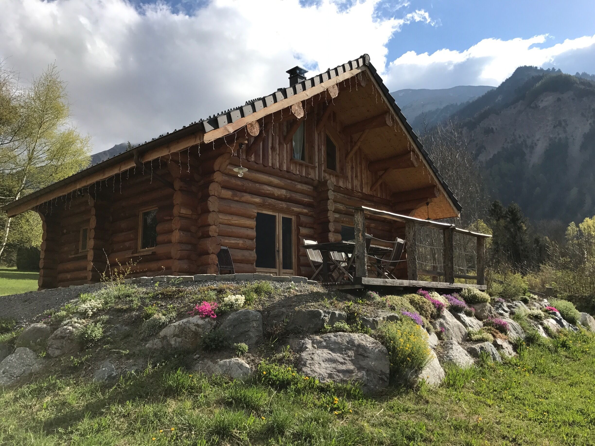 A wooden log cabin with a porch, surrounded by a mountainous landscape.