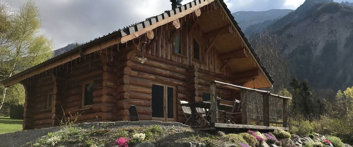A wooden log cabin with a porch, surrounded by a mountainous landscape.