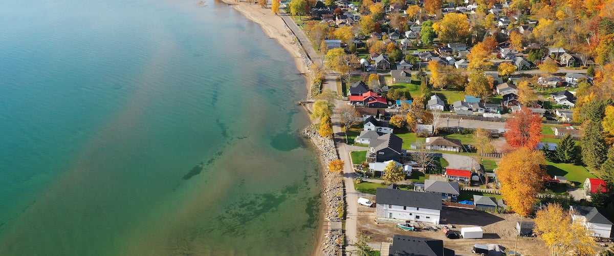 A coastal town with houses along a beach, surrounded by autumn-colored trees.