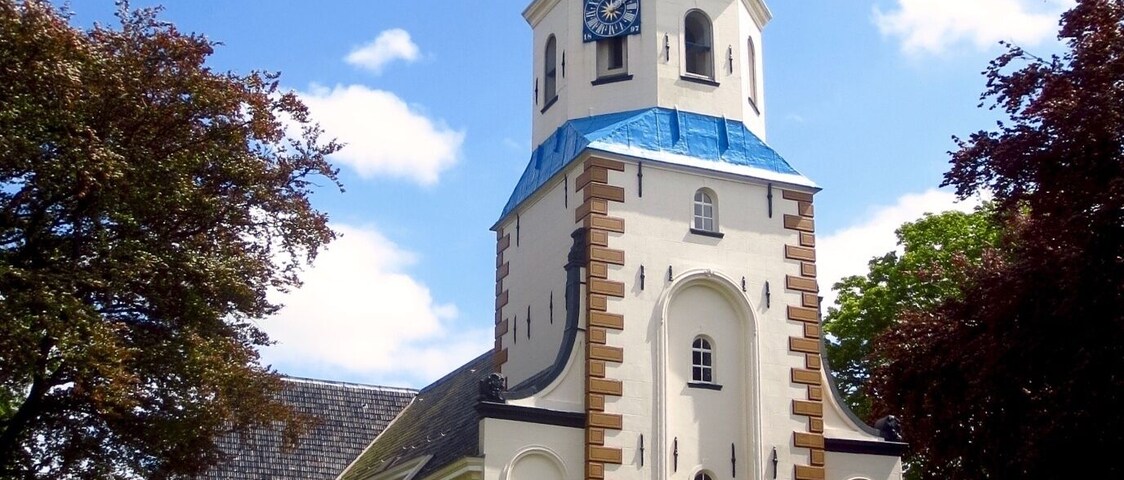 Una iglesia con un alto campanario, una cúpula azul y paredes blancas.