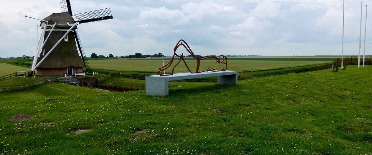 Un moulin à vent, un banc et une sculpture dans un champ d’herbe.