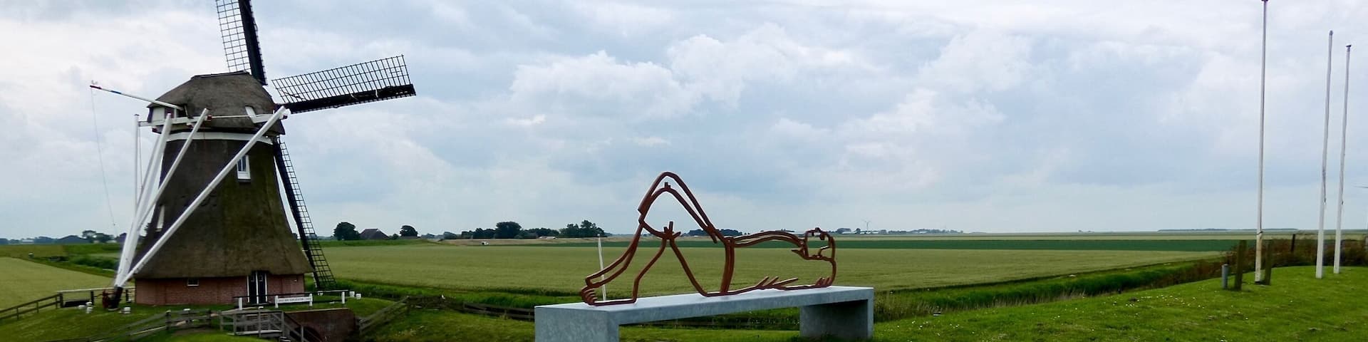 A windmill, a bench, and a sculpture in a grassy field.