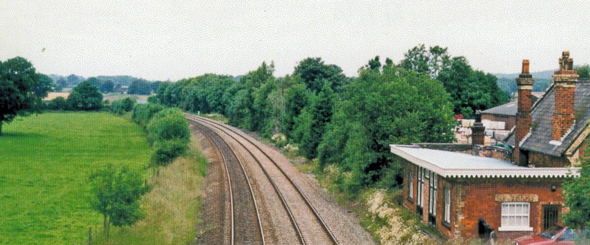 A railway track curving through a green field, with a brick building and trees in the background.