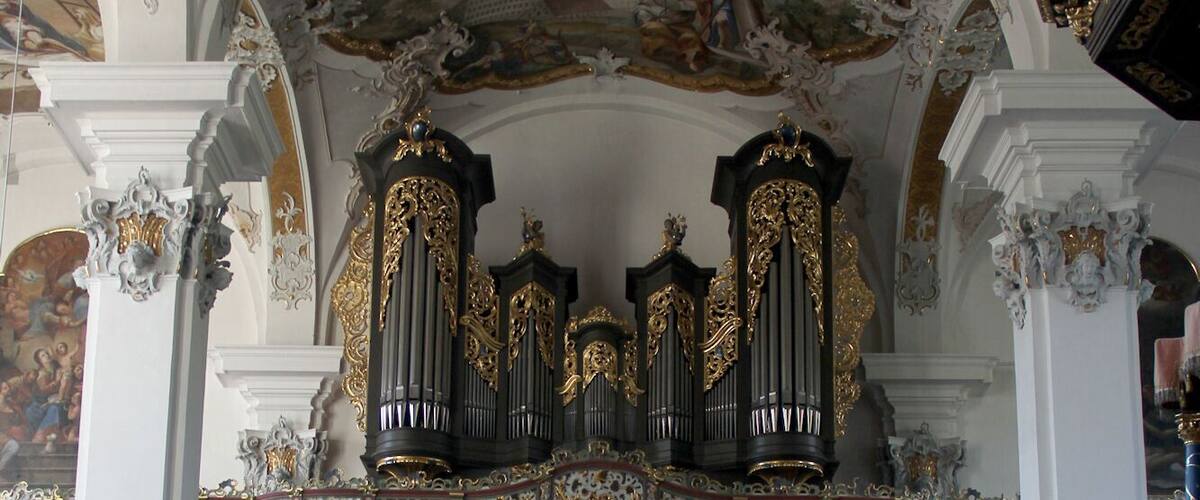 An ornate church interior with a high ceiling, detailed frescoes, and a large pipe organ.