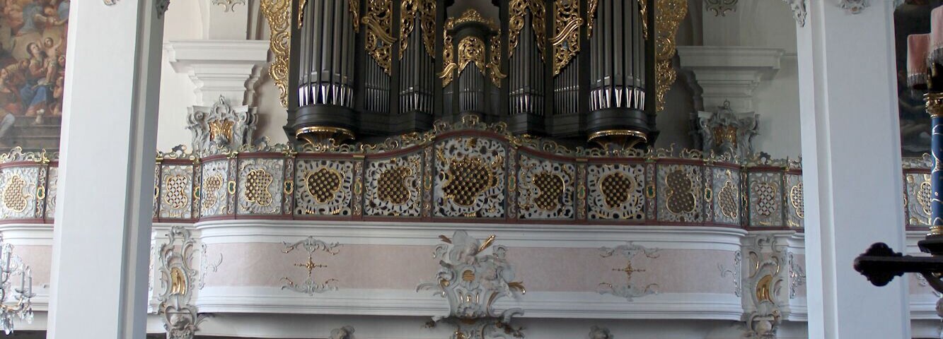 An ornate church interior with a high ceiling, detailed frescoes, and a large pipe organ.