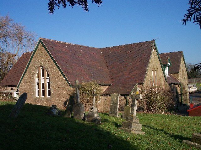 A church with a red roof and stone walls, surrounded by a cemetery with headstones.