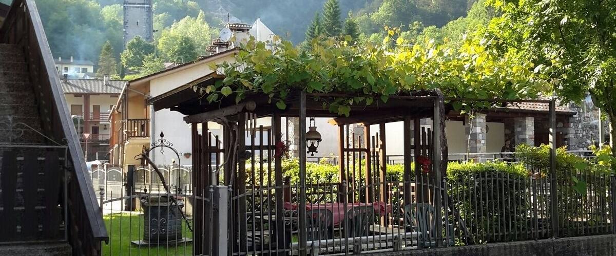 A gazebo with vines, a clock tower, and mountains in the background.