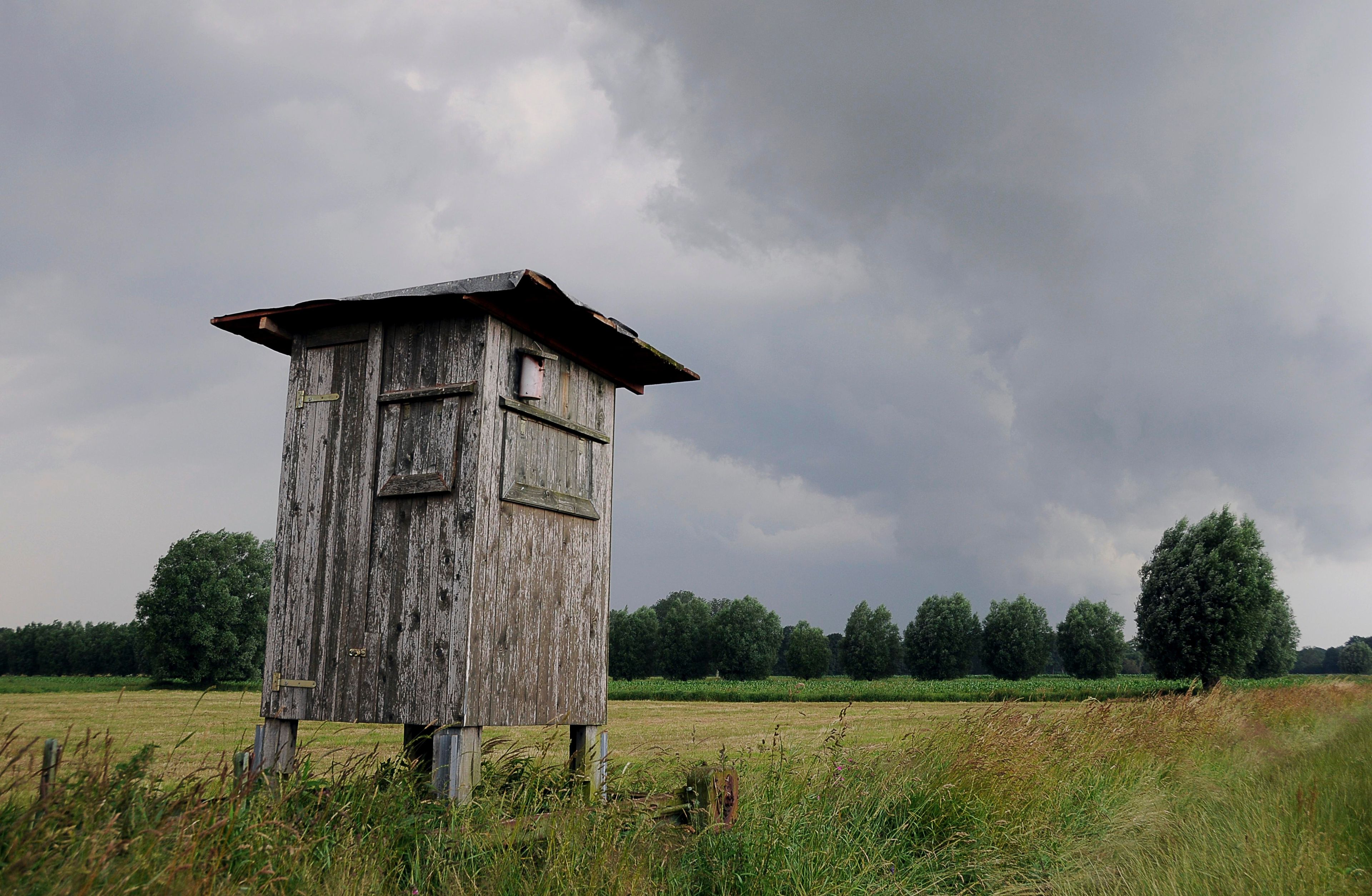 A weathered wooden structure in a field with a cloudy sky.