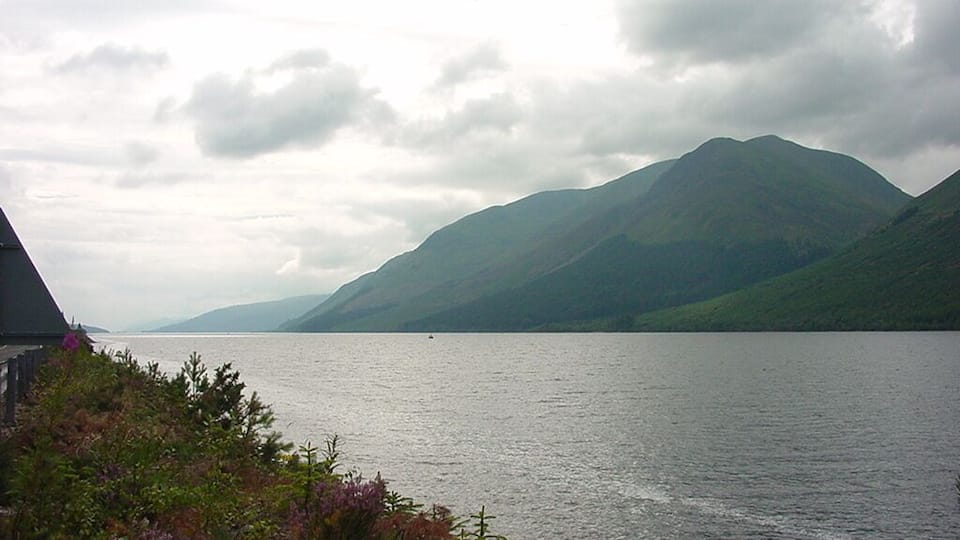 A lake with mountains in the background and a wooden structure on the left.