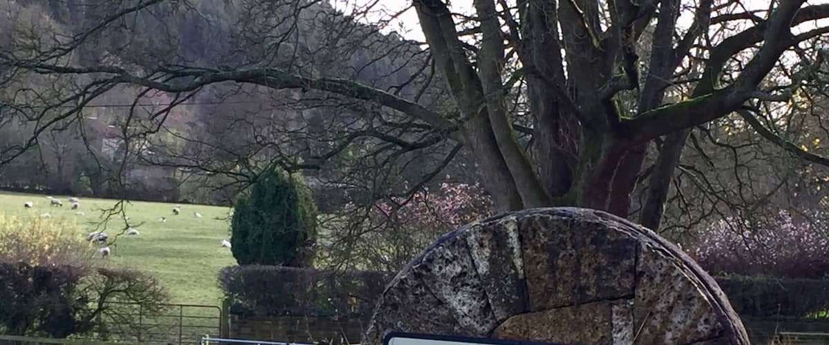 A rural landscape with a sign reading "Oldstead" mounted on a stone post.