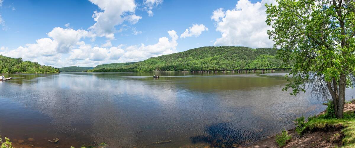 A calm lake with a wooden pier, surrounded by lush green hills and a clear blue sky.
