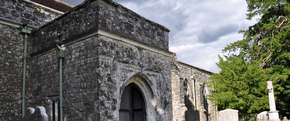An old stone building with a large arched entrance, surrounded by a cemetery with headstones.