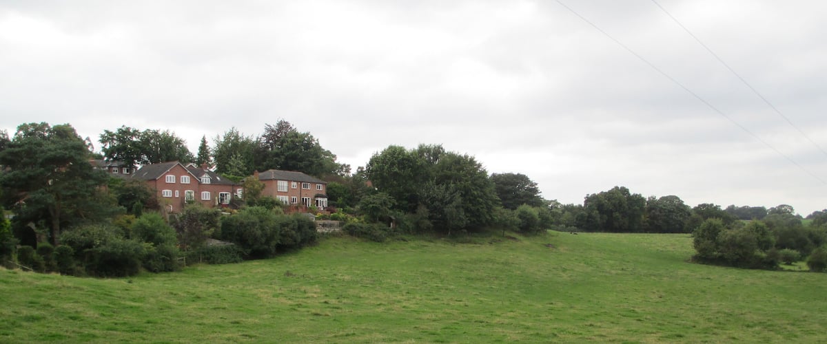 A grassy field with a red house and trees in the background.