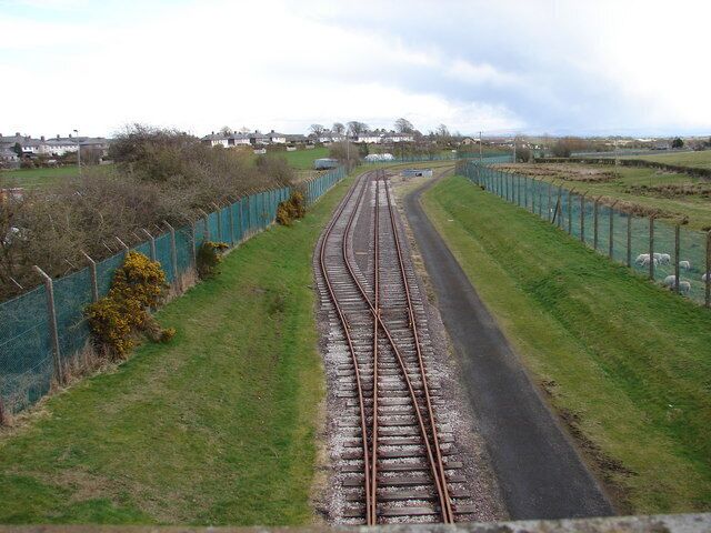 Railway tracks curving through a rural landscape with green fields and a fence along one side.