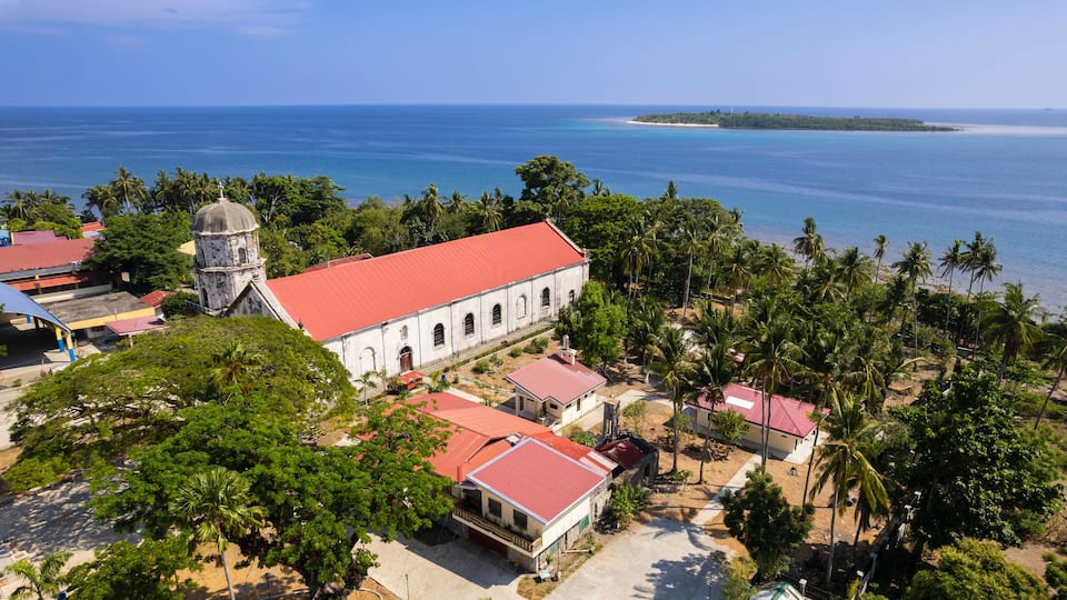 A coastal town with a prominent white church, palm trees, and a view of the ocean.